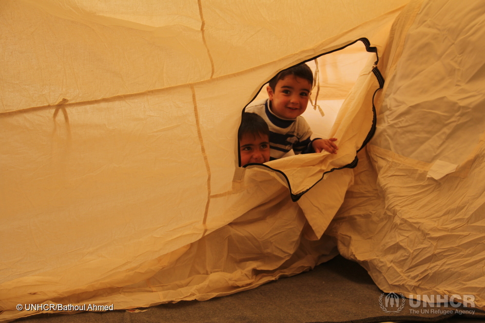 Two young Iraqi boys, their family displaced by the fighting in Mosul, peek out through the zipper of their tent at Hasansham camp, as UNHCR delivers cold weather supplies, including warm blankets and stoves. ; After two years trapped inside Iraq's second largest city, thousands of Iraqis are relieved to be free of tyrannical militant rule. But with the onset of winter and temperatures beginning to fall, UNHCR must now deliver life-saving cold weather equipment to millions of displaced Iraqis and Syrians. In preparation for the military operation in Mosul which began in October 2016, UNHCR pre-planned the construction of 11 new camps, designed to accommodate 120,000 people. Emergency plans are also in place to provide tents and supplies to those who cannot access the camps. Around 3.3 million Iraqis, ten per cent of the population, have fled their homes since March 2014. © UNHCR/Photographer